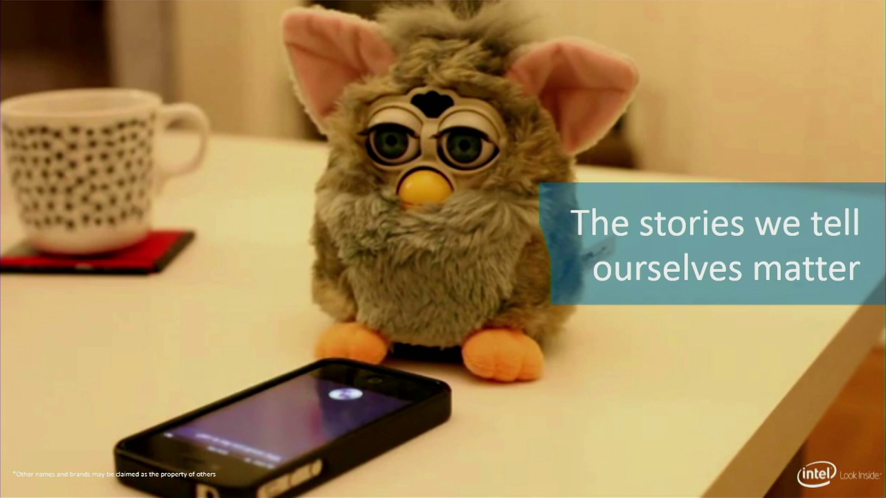 A Furby toy standing near an iPhone on a tabletop. Captioned "The stories we tell ourselves matter"