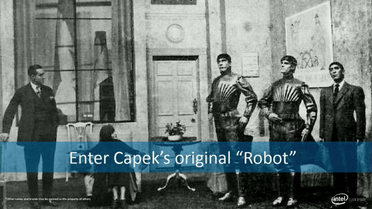 Several people standing in a drawing room, two costumed to suggest they are mechanical. Captioned "Enter Čapek's original robot"