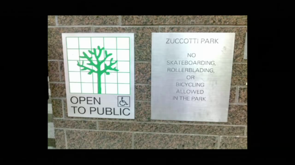 A "publicly-owned public space" sign, next to another with text reading "Zuccotti Park; No skateboarding, rollerblading, or bicycling allowed in the park"
