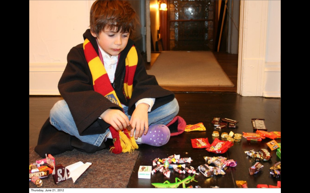 A young boy sitting cross-legged on the floor with a pile of various candies in front of him.