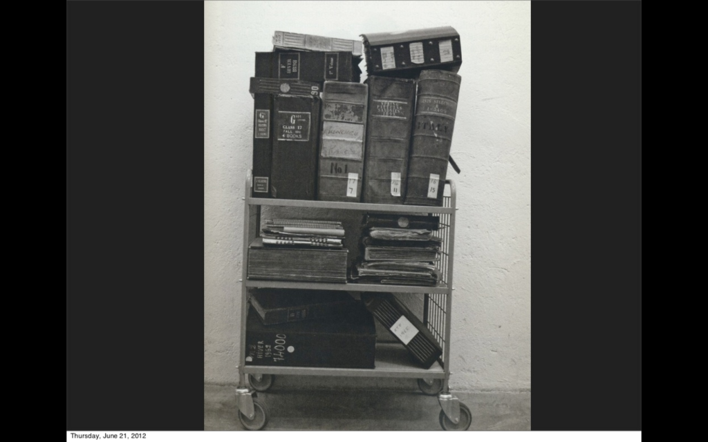 A rolling shelf with many large, old-looking binders on it.