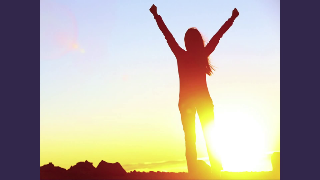 A woman, backlit by the sun, with arms raised in success
