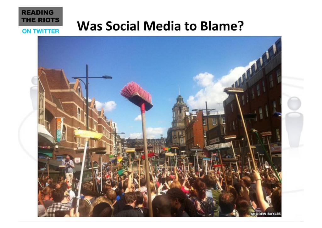 A large crowd of people standing in the street holding brooms in the air, bristles up.