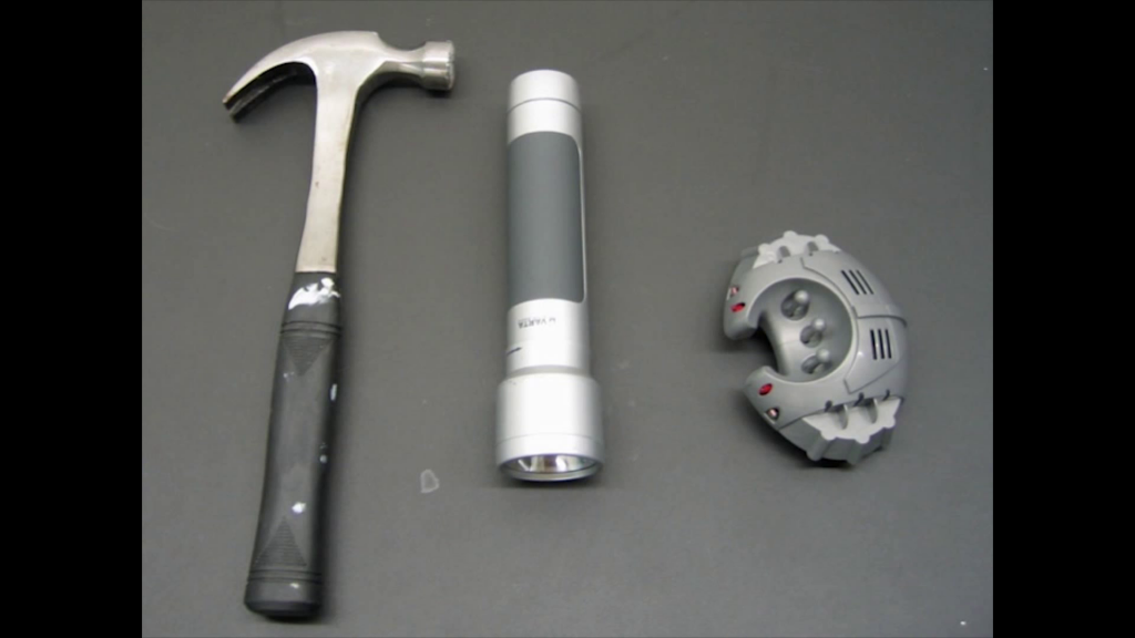 A hammer, flashlight, and small robotic toy laid out on a tabletop.