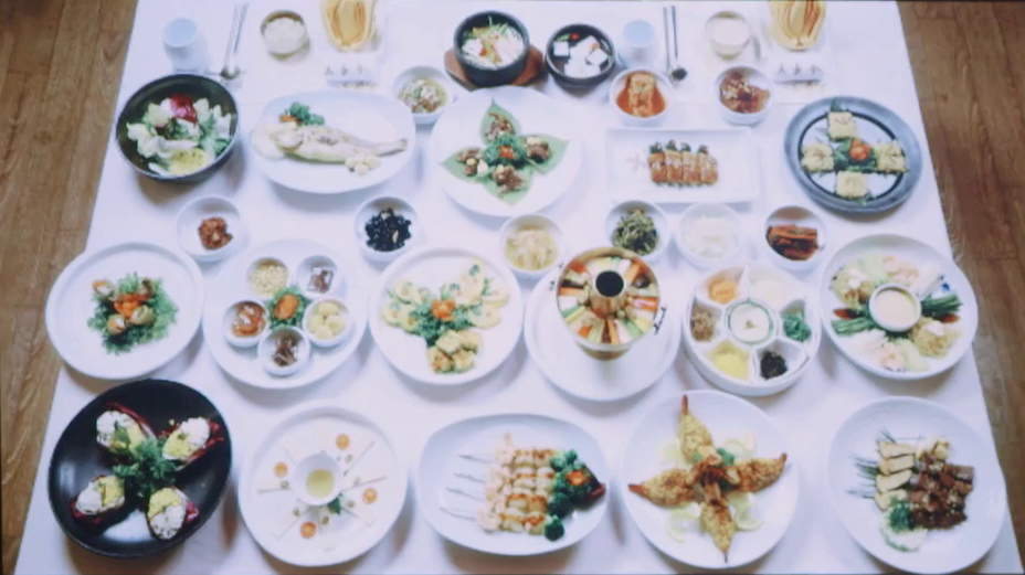 A dinner table covered with a large number of dishes ranging in size from entrees to collections of small bowls with pickles in them. 