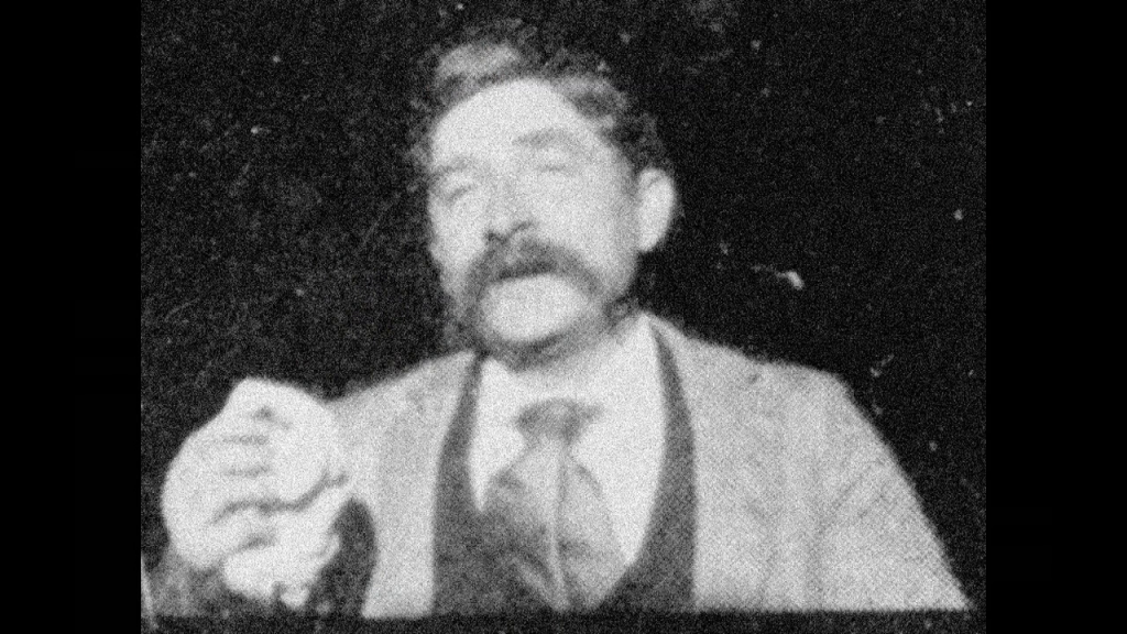 Grainy image of a man holding a handkerchief, with his eyes closed and mouth slightly open