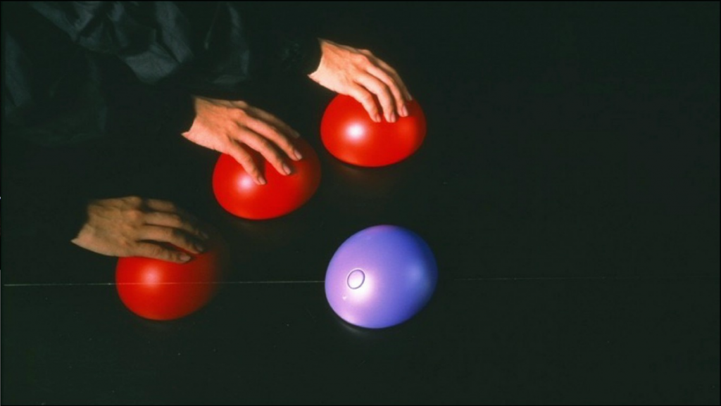 Three hands placed on a red, round object