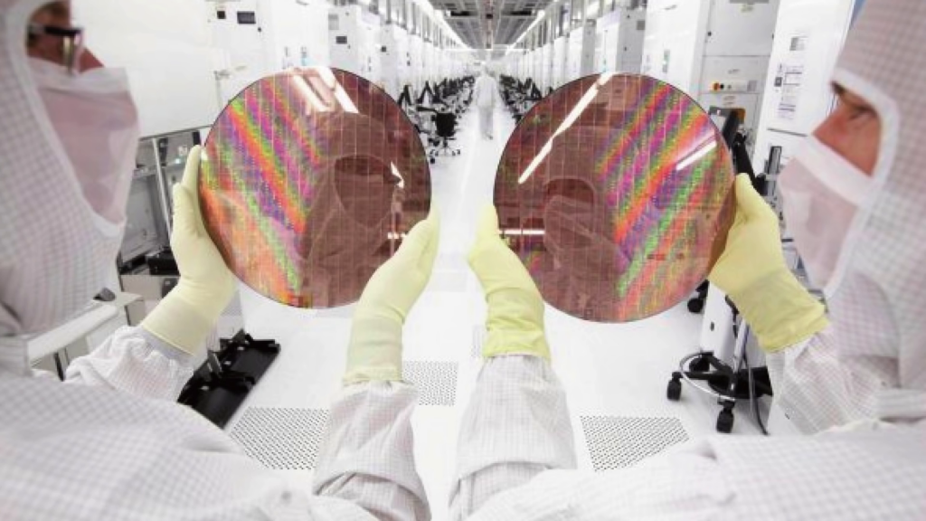 Photo from behind of two people holding large silicon wafers from which computer chips will be cut; their faces are reflected in the wafers