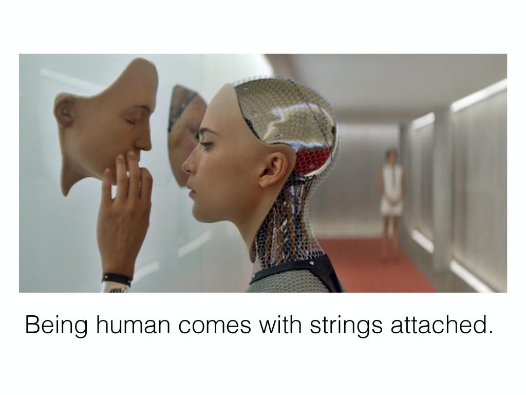 The Ava robot from the movie Ex Machina touching another face hanging on a wall.