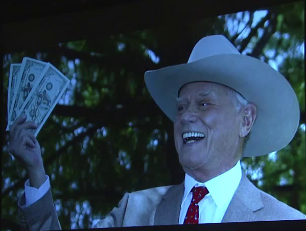 JR Ewing from the TV show Dallas laughing and holding  a handful of money