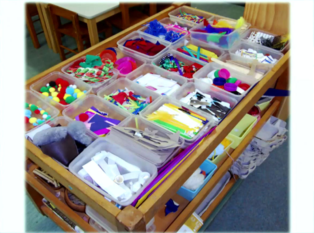 A childrens' crafts table covered in plastic bins filled with various colorful materials