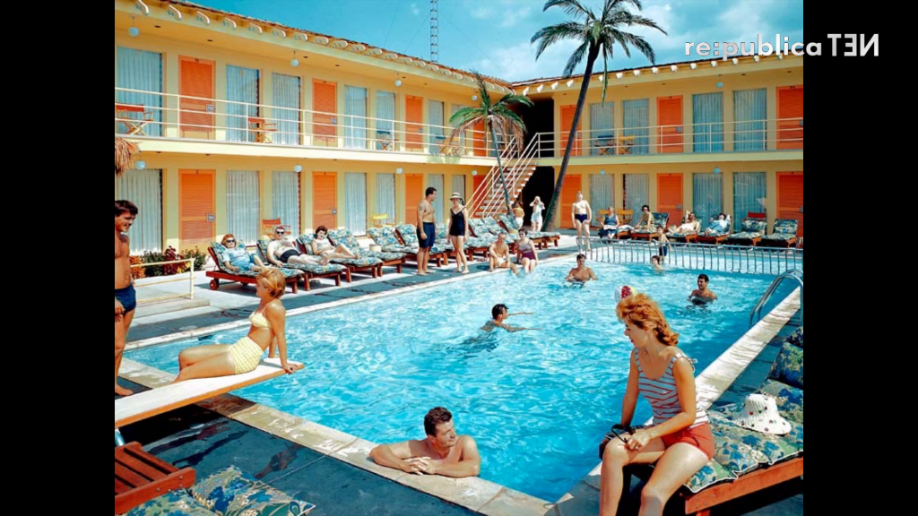 Many people lounging around and swimming in a pool at a hotel.