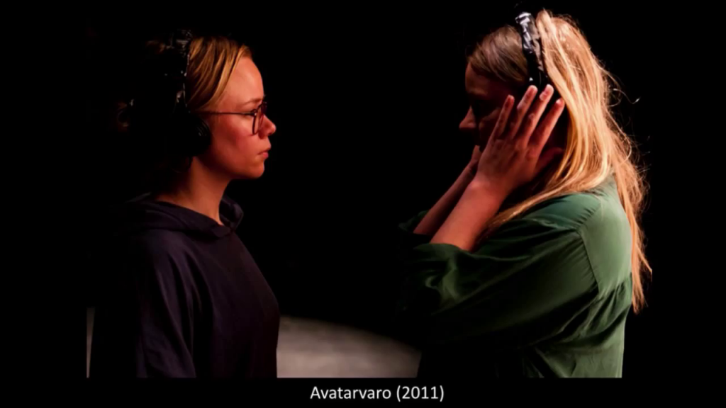 Two women stand closely facing each other, wearing headphones