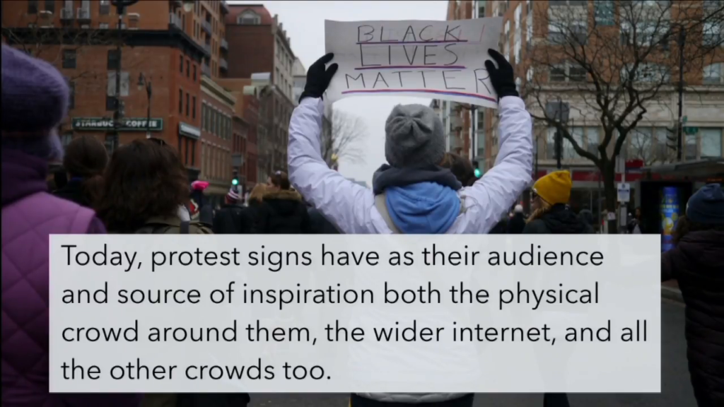 Photo of a woman from behind, holding a protest sign on which "Black Lives Matter" can be read by people behind her.