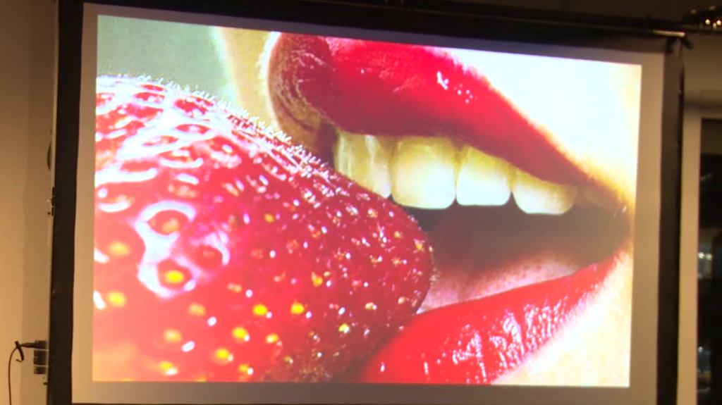 Closeup of a woman's mouth wearing red lipstick, about to bite into a strawberry