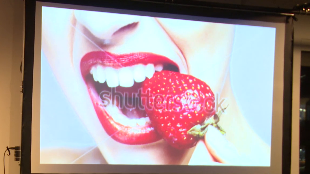 A different photo a woman's mouth wearing red lipstick, about to bite into a strawberry