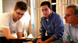 Edward Snowden, Glenn Greenwald, and another man seated around and looking at a small computer screen