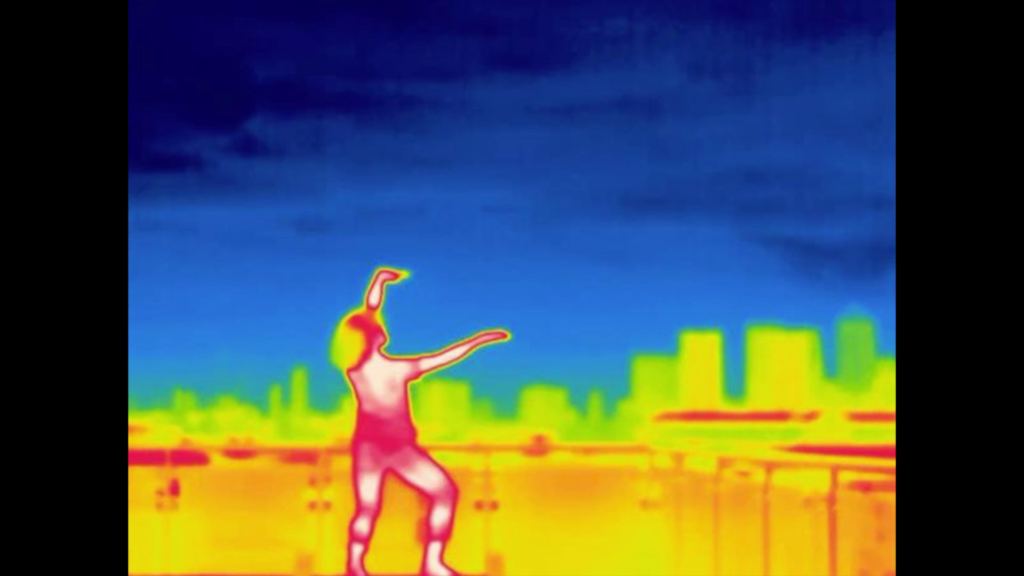 Infrared image of a dancer on a rooftop, a skyline visible in the distance