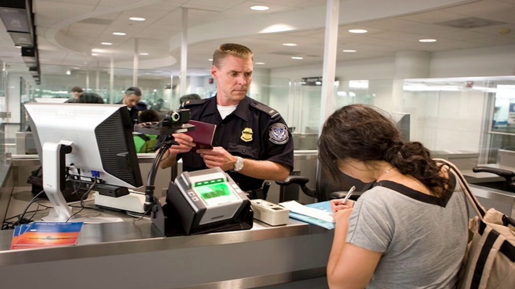 A woman signing paperwork while an airport customs officer looks on