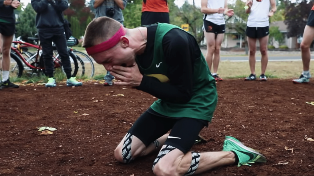 Justin Gallegos, wearing running gear and kinesio tape around his legs, kneeling on the ground seeming to cry into his hands.