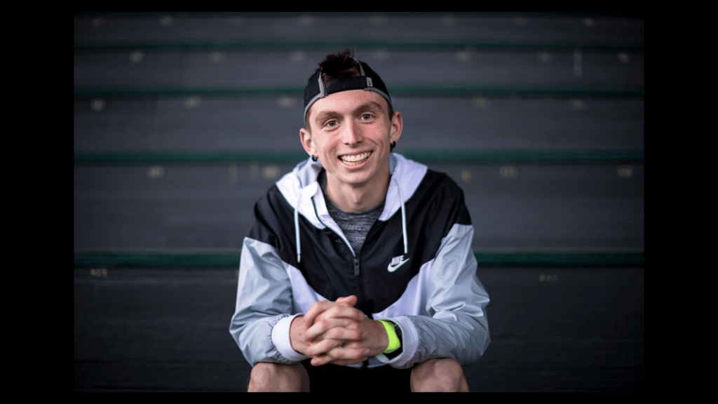 Justin Gallegos seated on bleachers, smiling at the camera.