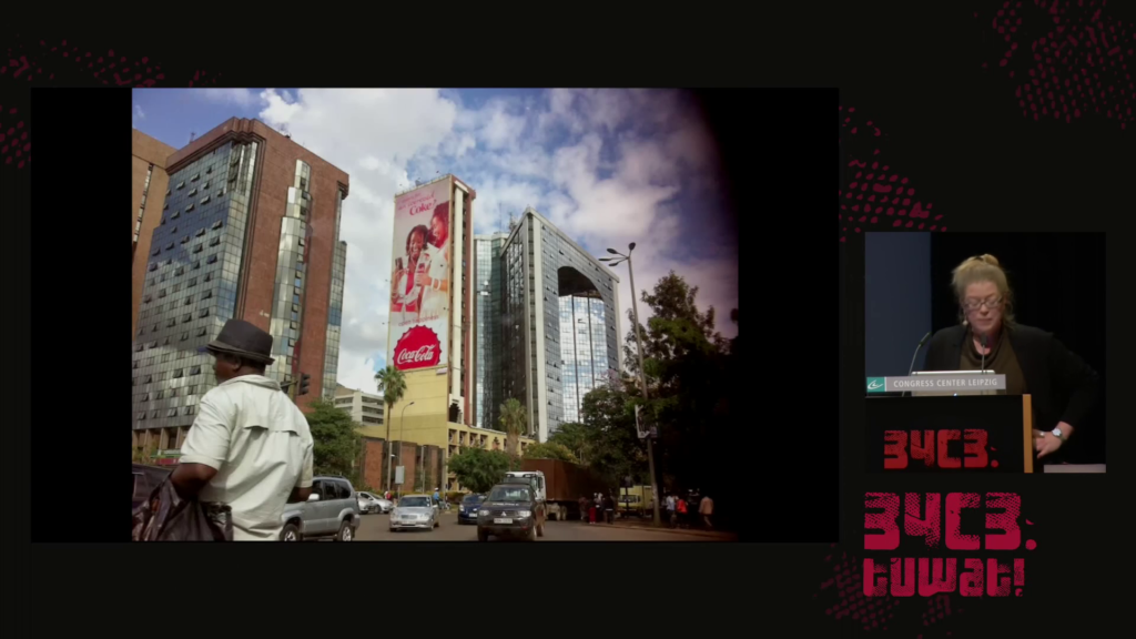 A street scene in Nairobi, several modern buildings with glass facades visible in the background, one with a multi-story Coca-Cola ad on one side