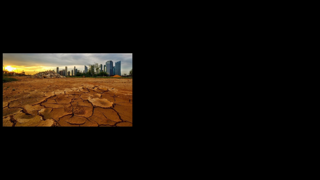 Photo from low to the ground, showing dry cracked dirt with a city skyline visible in the distance
