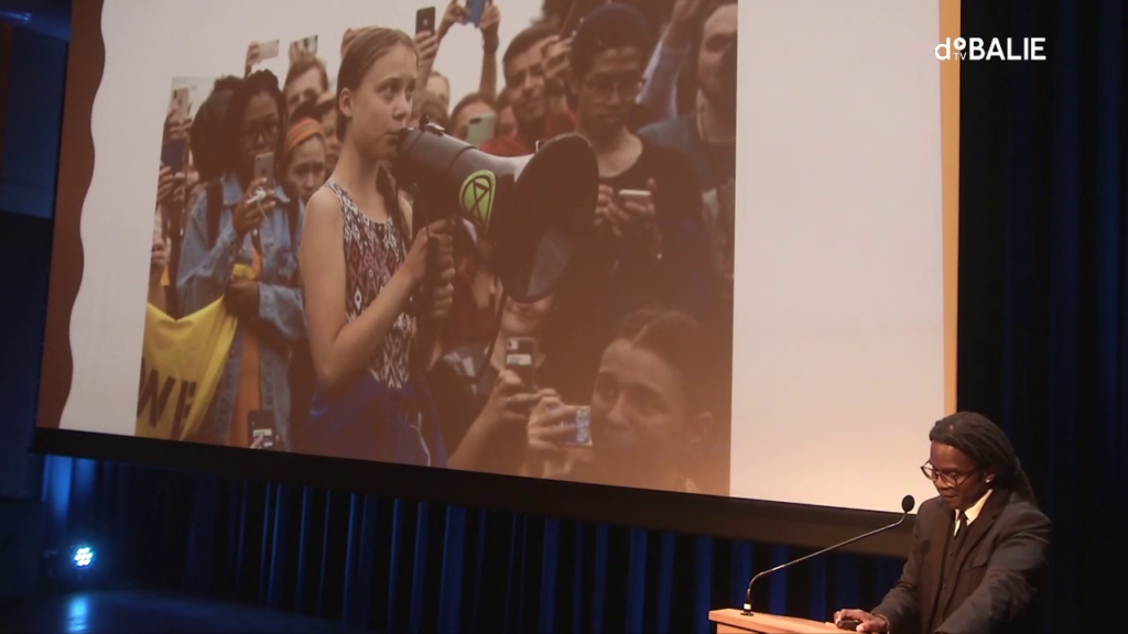 Greta Thunberg speaking into a megaphone, surrounded by a large crowd of people